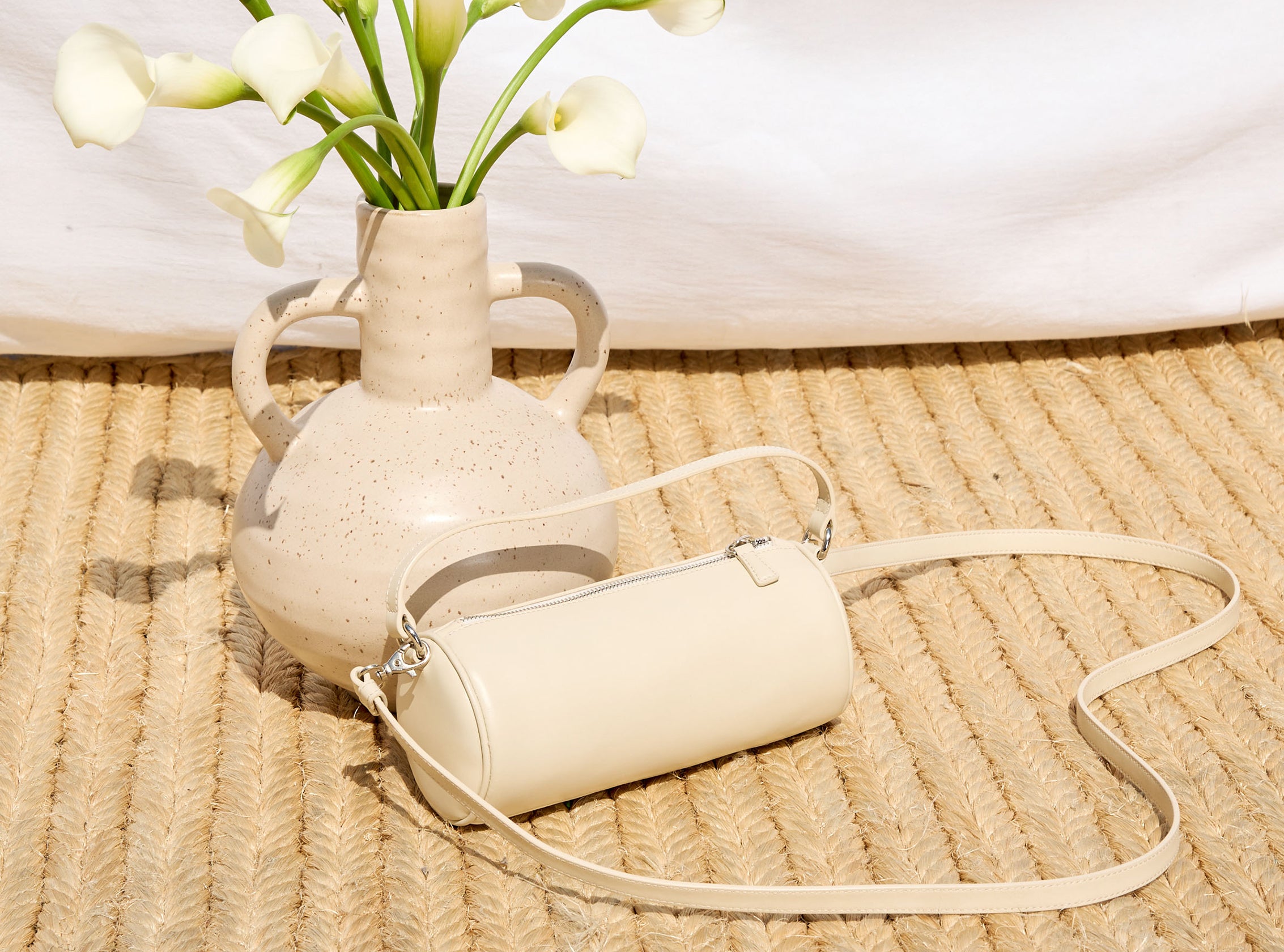 Beige handbag next to a vase with white flowers on a woven surface