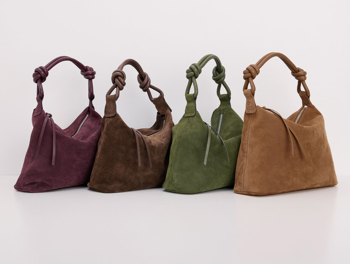 Four suede shoulder bags in plum, taupe, olive green, and camel brown, arranged in a row on a clean white background.