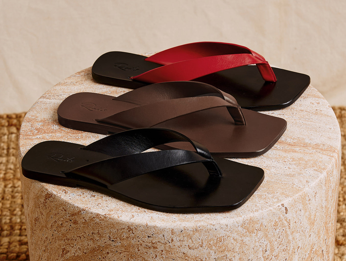 Three pairs of black, brown, and red flip-flops on a textured surface.
