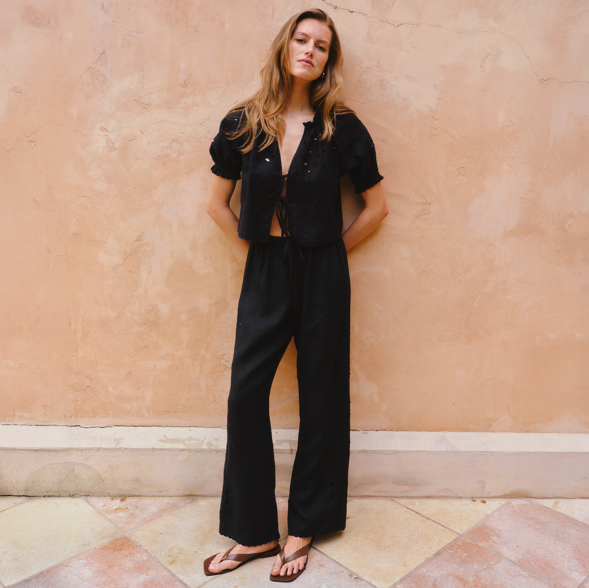 Woman wearing a black outfit against a peach-colored wall.