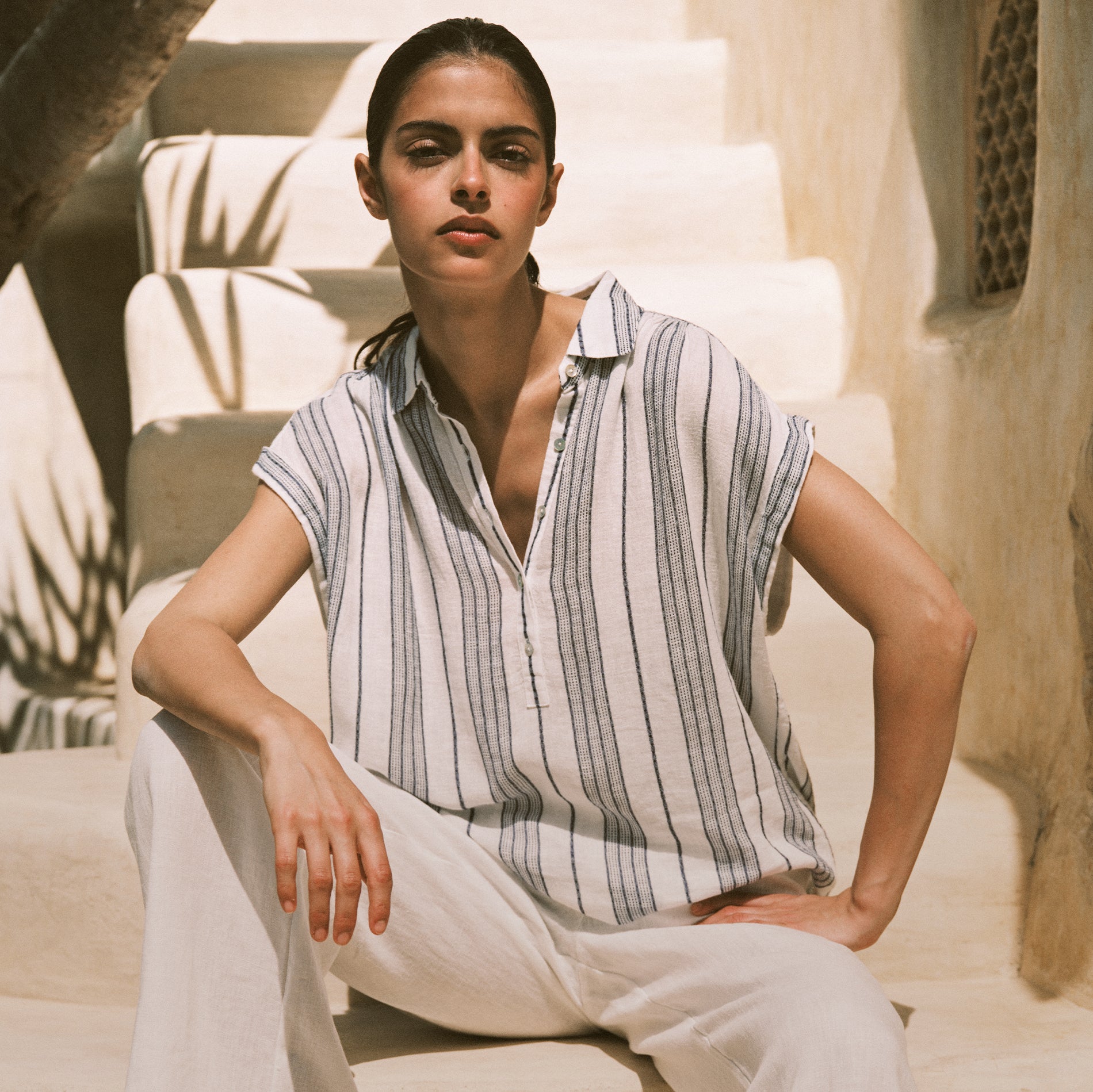 Woman wearing a striped shirt and white pants sitting on a staircase.