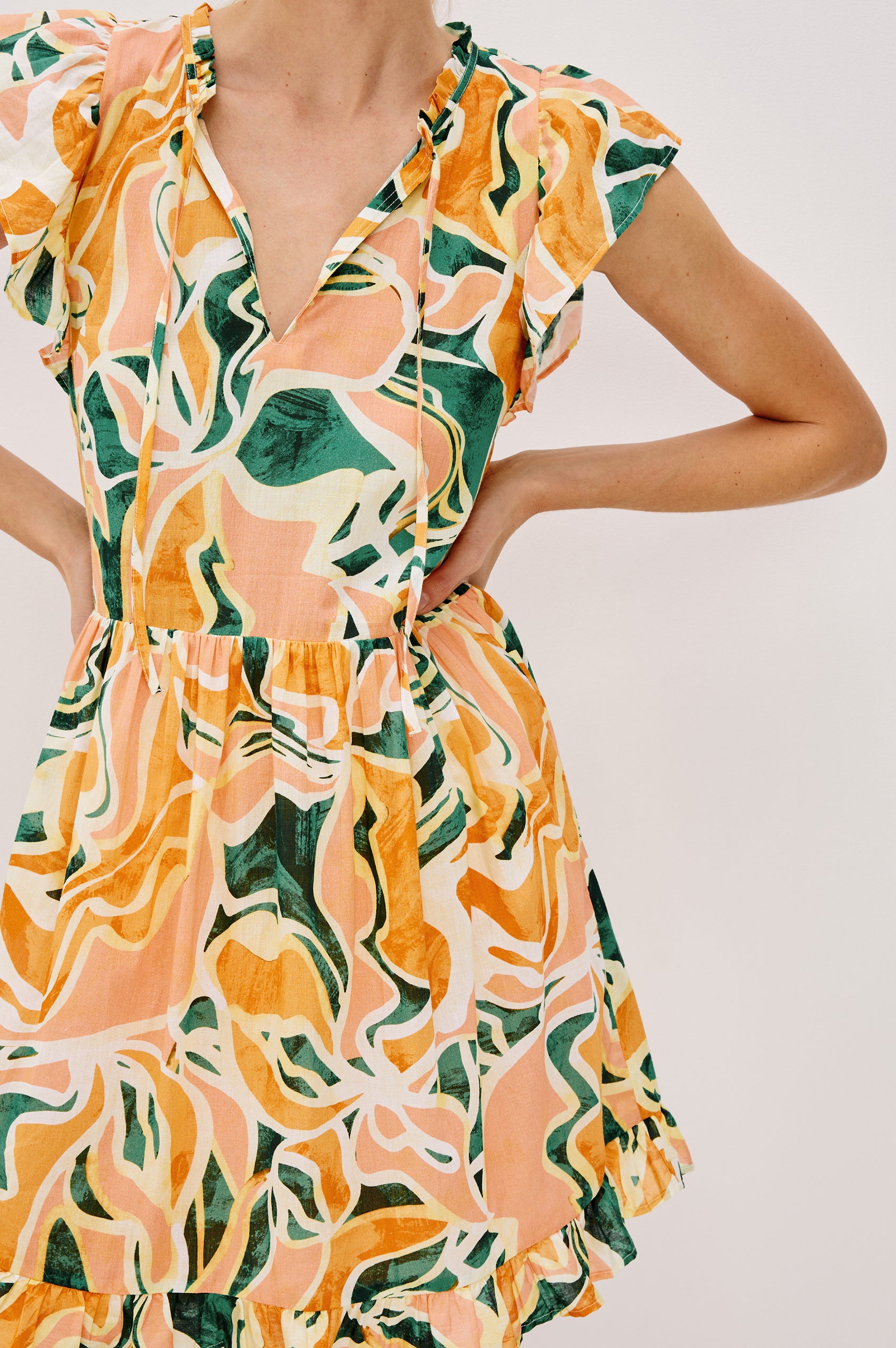 Zinnia Popover Mini Dress with Short Flutter Sleeves, Small Ruffle at Neck, V-Front with Self Tie Closure, Ruffle Hem in Tulum Colorway. Front Detail  View Shown on Model.