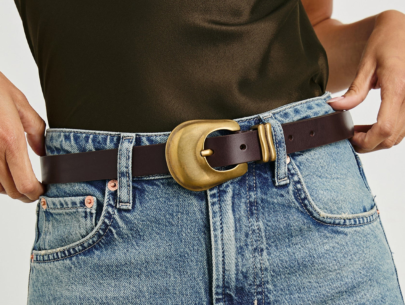 Person wearing blue jeans with a brown belt and gold buckle.