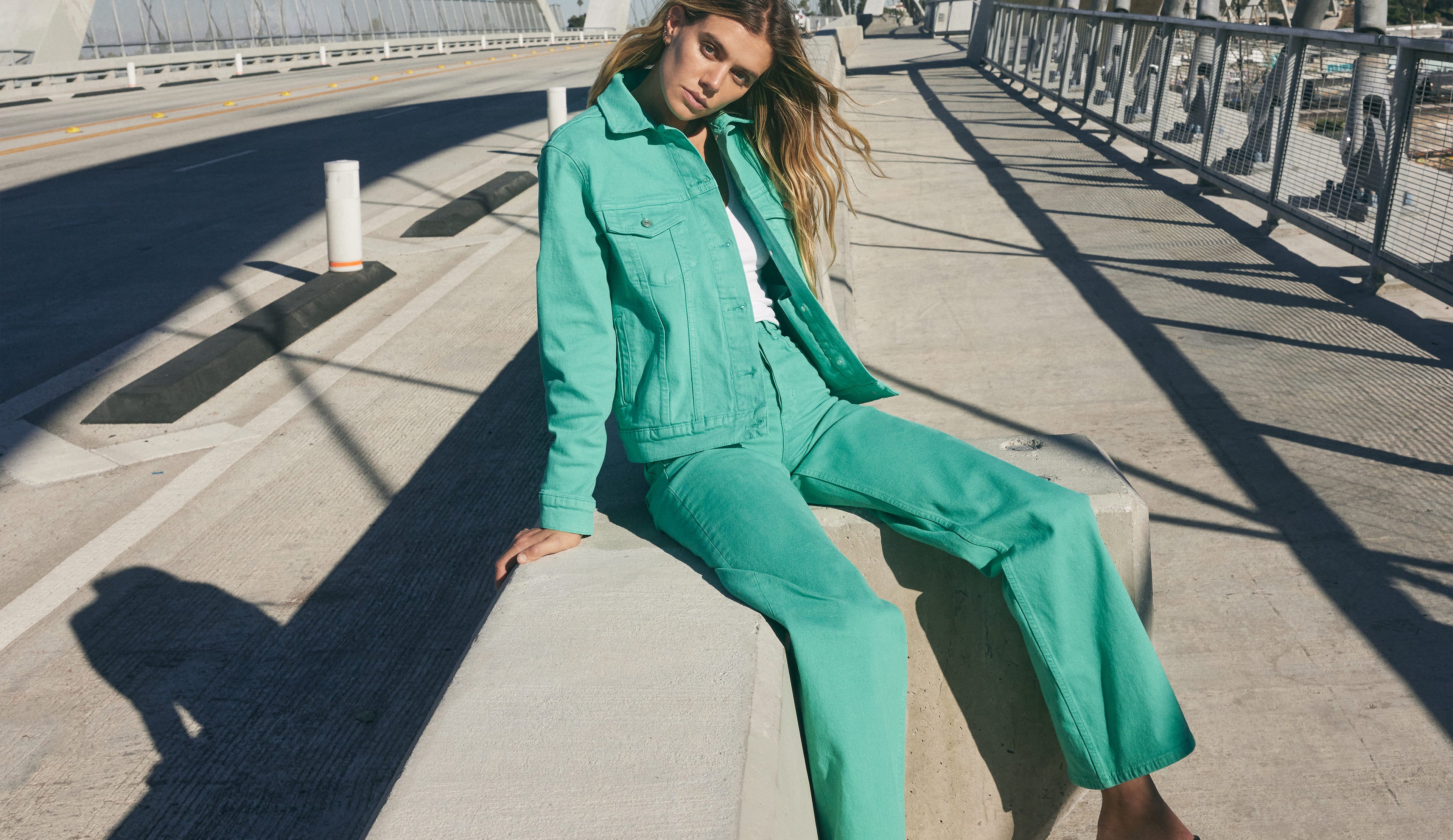 EDITORIAL IMAGE OF MODEL SITTING DOWN WEARING GETTY WIDE LEG JEANS AND MULHOLLAND JACKET IN EMERALD
