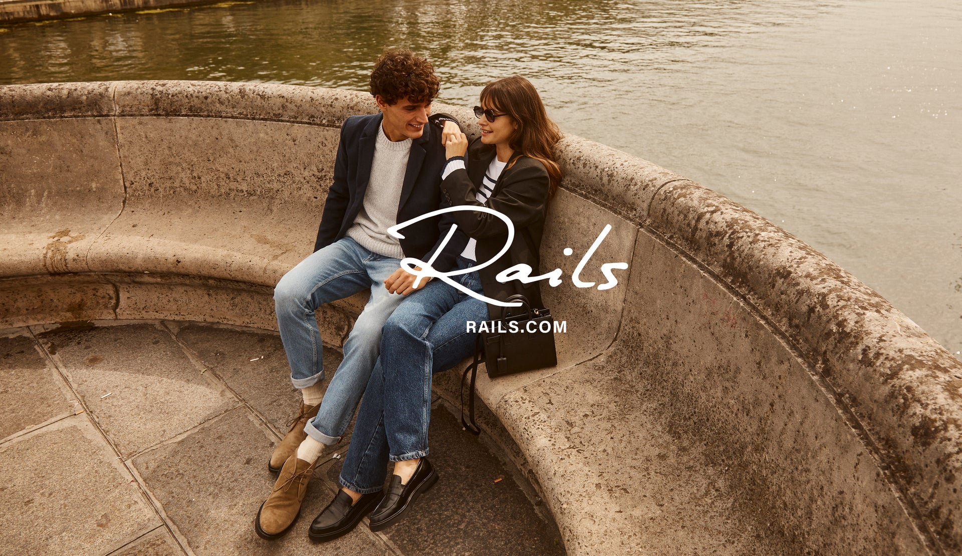 EDITORIAL IMAGE OF TWO MODELS SITTING OUTSIDE. FRIST MODEL IS WEARING LARK COAT, DONOVAN SWEATER, AND CLAYTON SLIM STRAIGHT JEANS. SECOND MODEL IS WEARING JAC BLAZER, GEMMA SWEATER, AND TOPANGA STRAIGHT JEANS. 