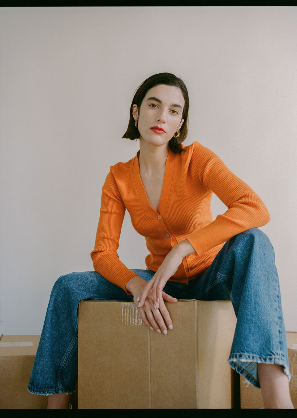 EDITORIAL IMAGE OF MODEL SITTING WEARING BEAU CARDIGAN IN TANGERINE AND SPEEDWAY 90S BOYFRIEND JEAN IN SLATE SKY