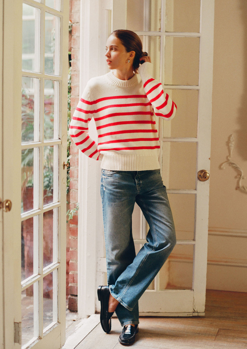 Woman wearing a red and white striped sweater and blue jeans standing in a doorway.