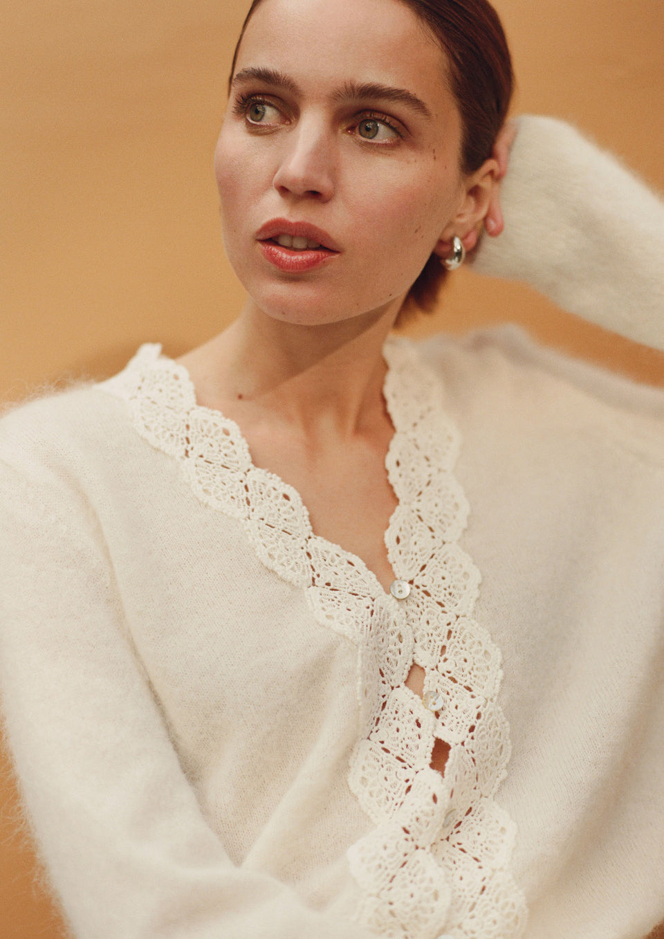 Woman wearing a white lace-trimmed sweater against an orange background.