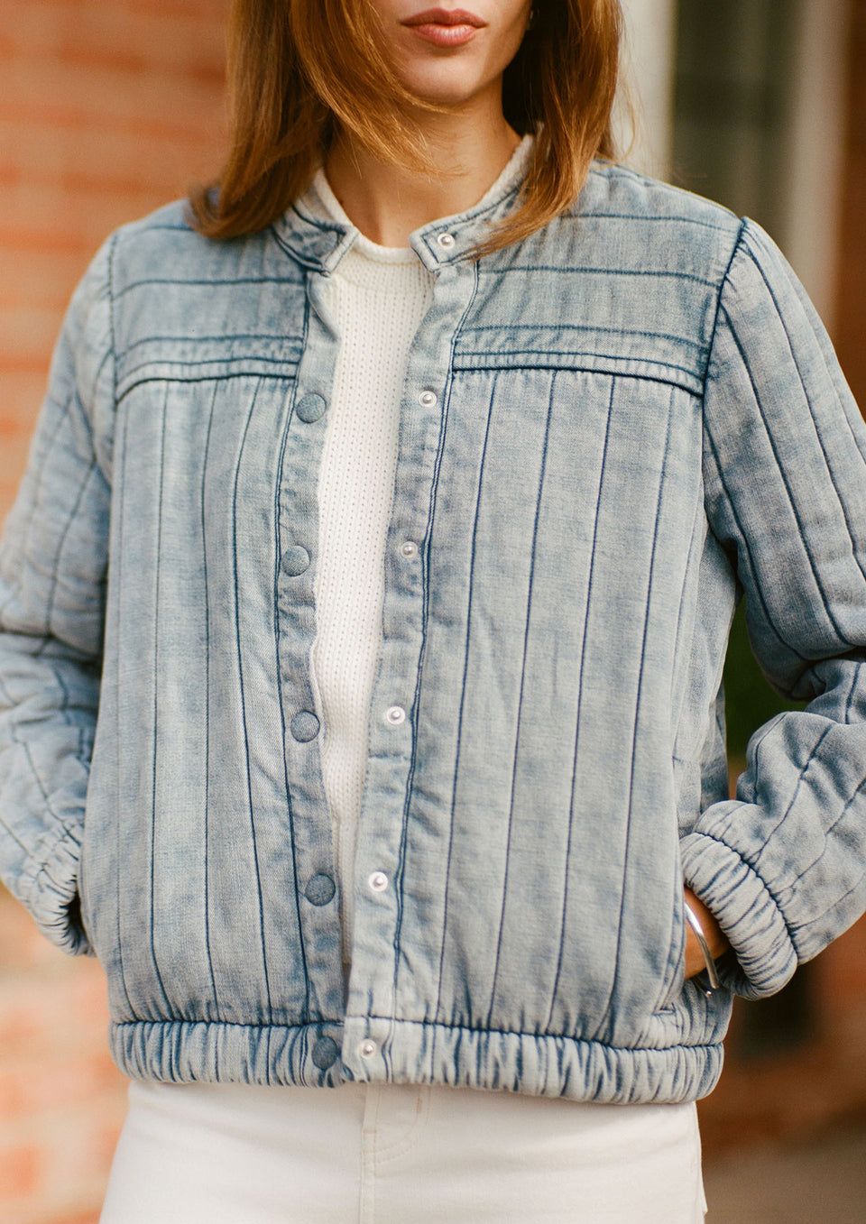 Woman wearing a light blue denim jacket with a blurred background.