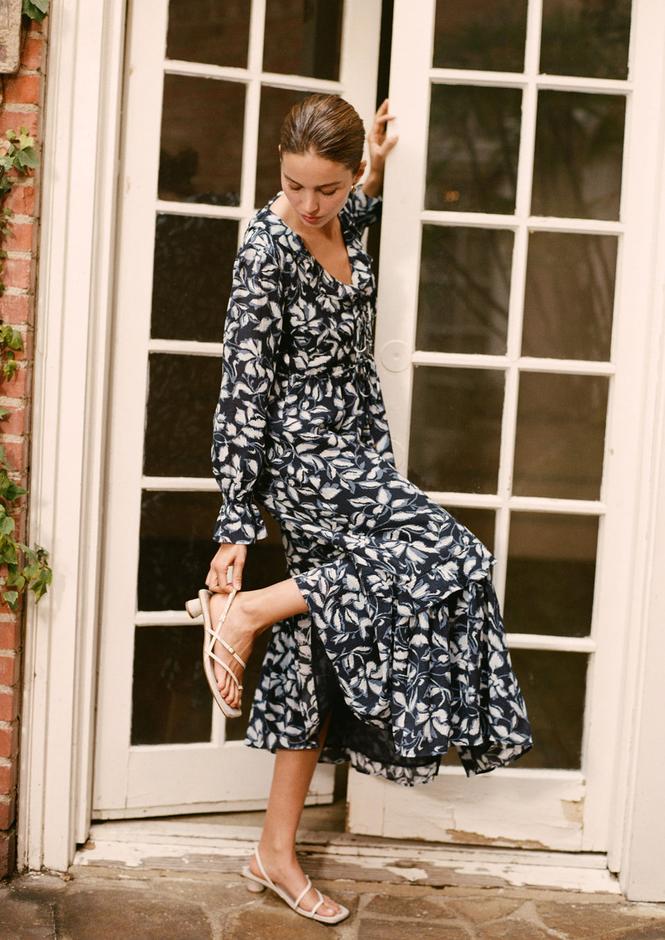 Woman in a blue floral dress standing in front of a door.