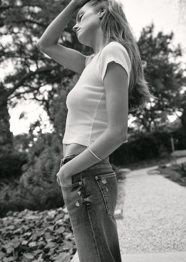 Woman wearing a white top and jeans standing outdoors with trees in the background