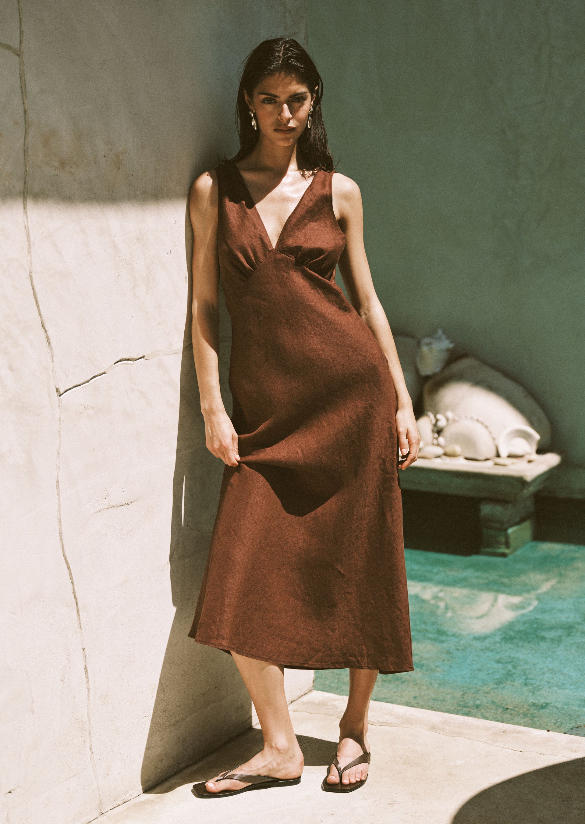 Woman in a brown maxi dress with brown sandals standing by a pool