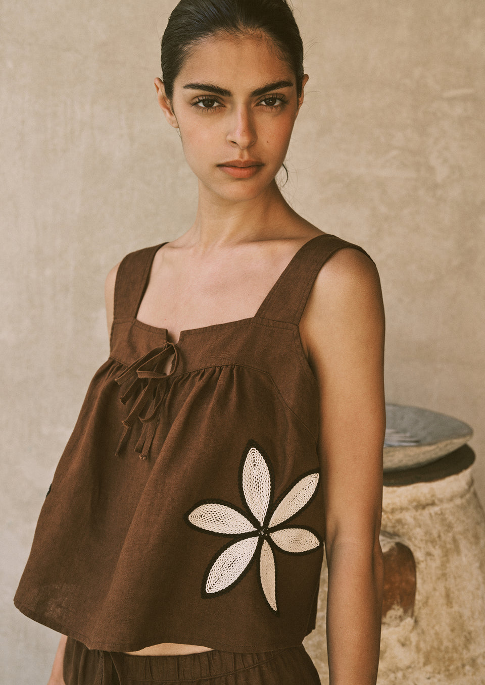Woman wearing a brown sleeveless top with a floral design against a neutral background