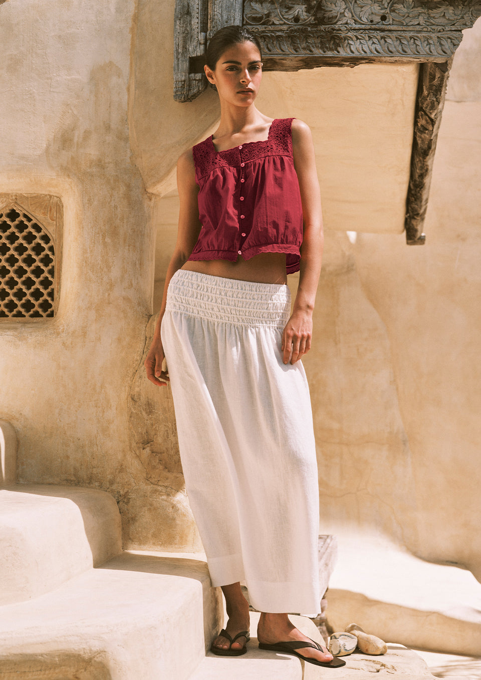 Woman wearing a red top and white skirt standing in front of a textured wall.