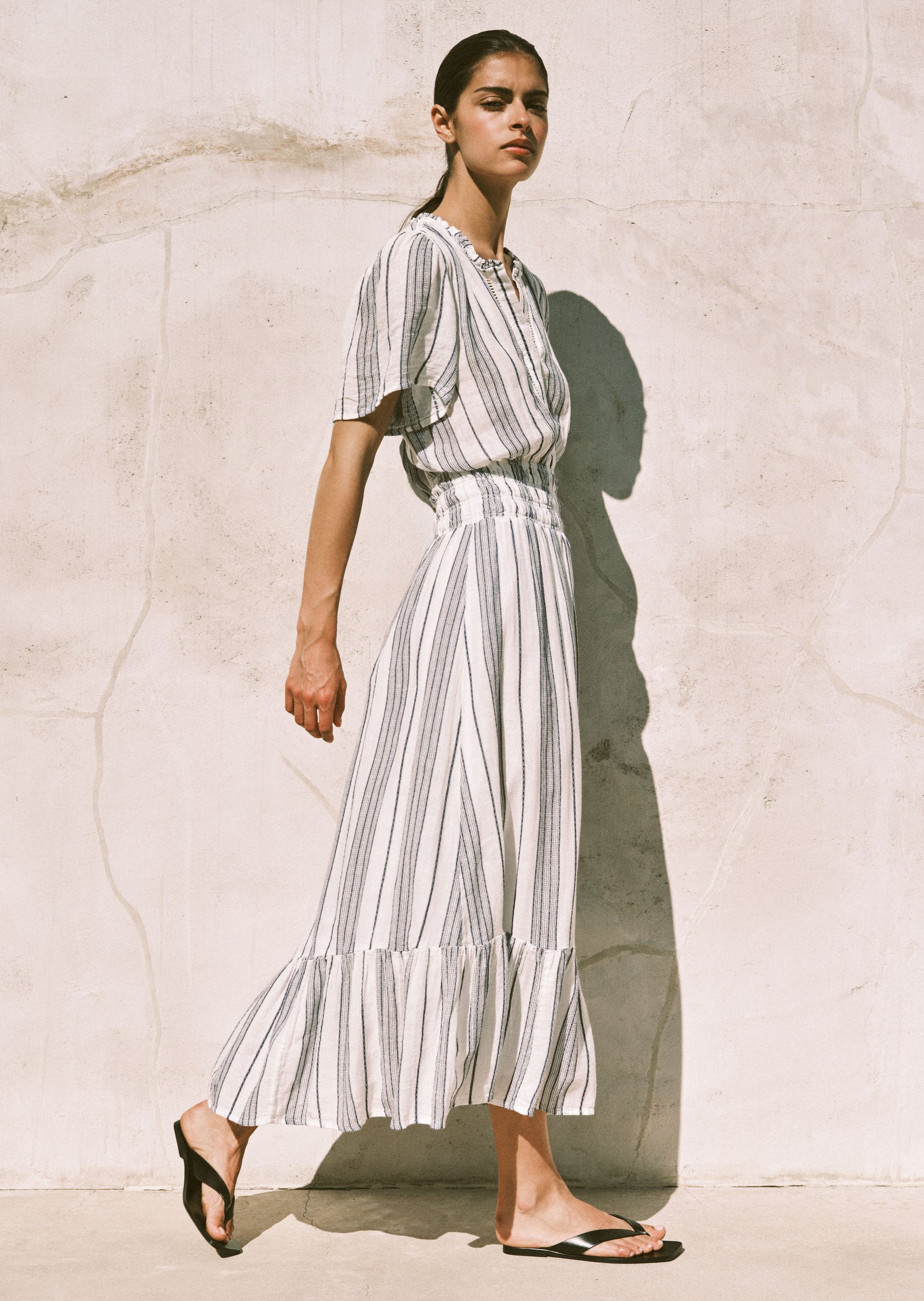 Woman wearing a long, striped dress against a light stone wall.