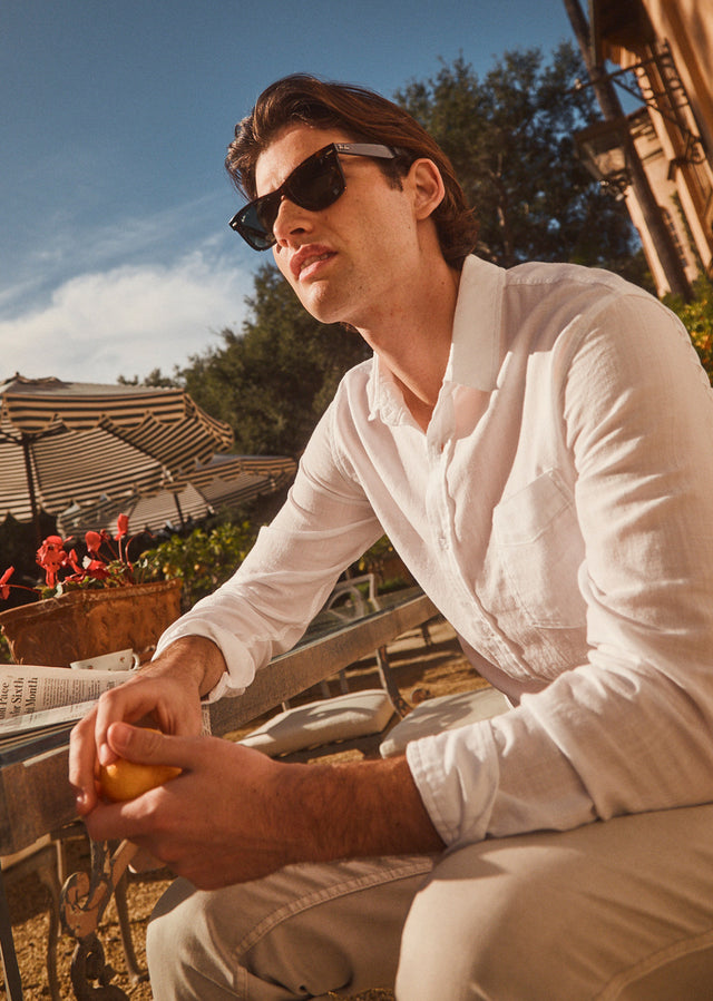 EDITORIAL IMAGE OF MODEL SITTING AND WEARING WYATT SHIRT IN WHITE AND CARVER PANT IN STONE