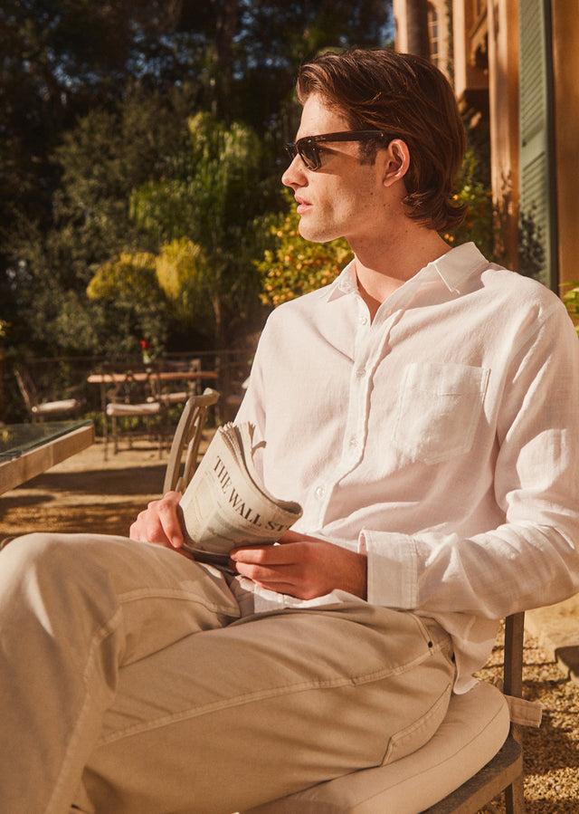 EDITORIAL IMAGE OF MODEL SITTING AND WEARING WYATT SHIRT IN WHITE AND CARVER PANT IN STONE