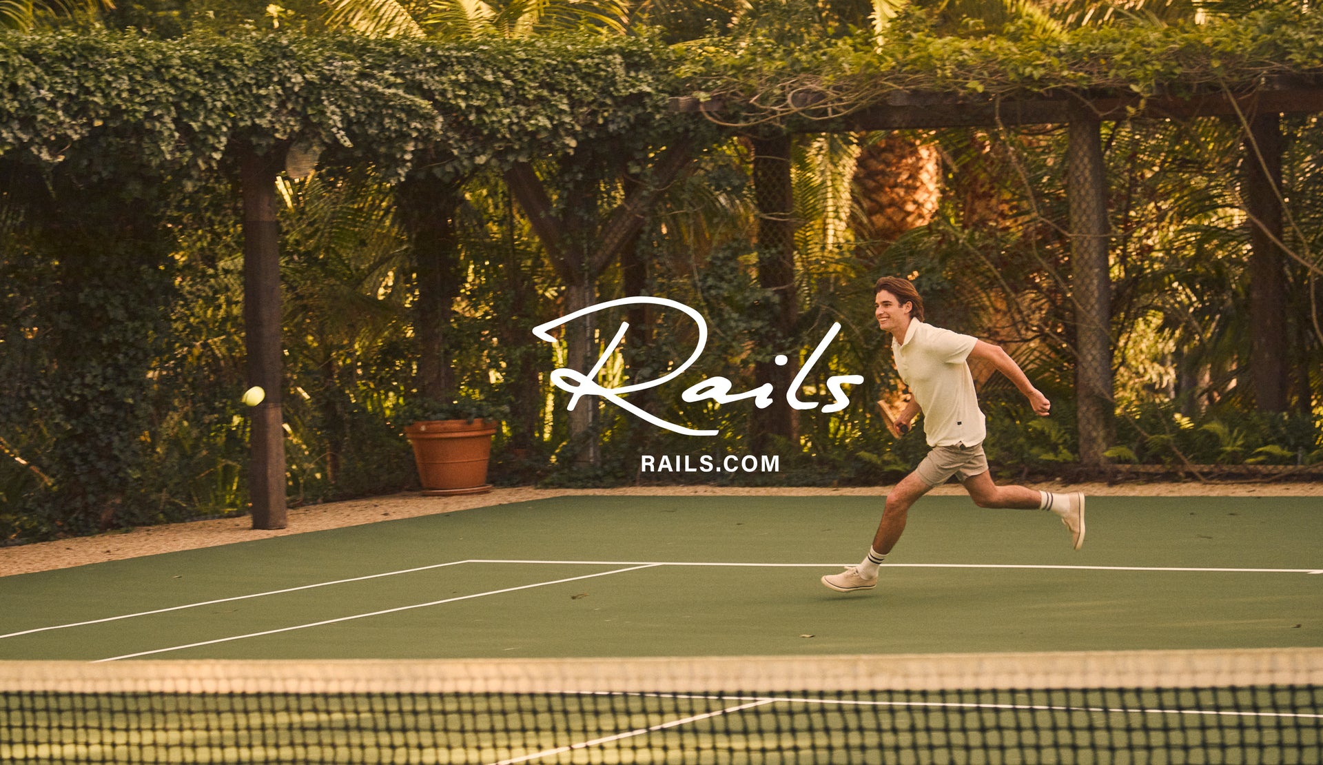 EDITORIAL IMAGE OF MODEL PLAYING TENNIS WEARING RHEN POLO SHIRT IN TERRY PEARL AND CRUZ SHORTS IN WASHED GREY