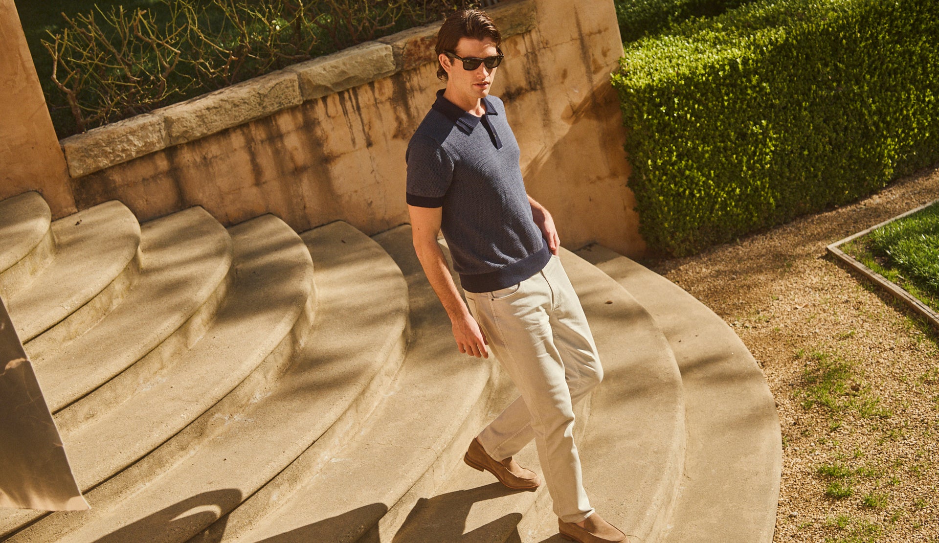 EDITORIAL IMAGE OF MODEL WEARING SHOREDITCH POLO SHIRT IN NAVY BROCADE AND CARVER PANT IN STONE