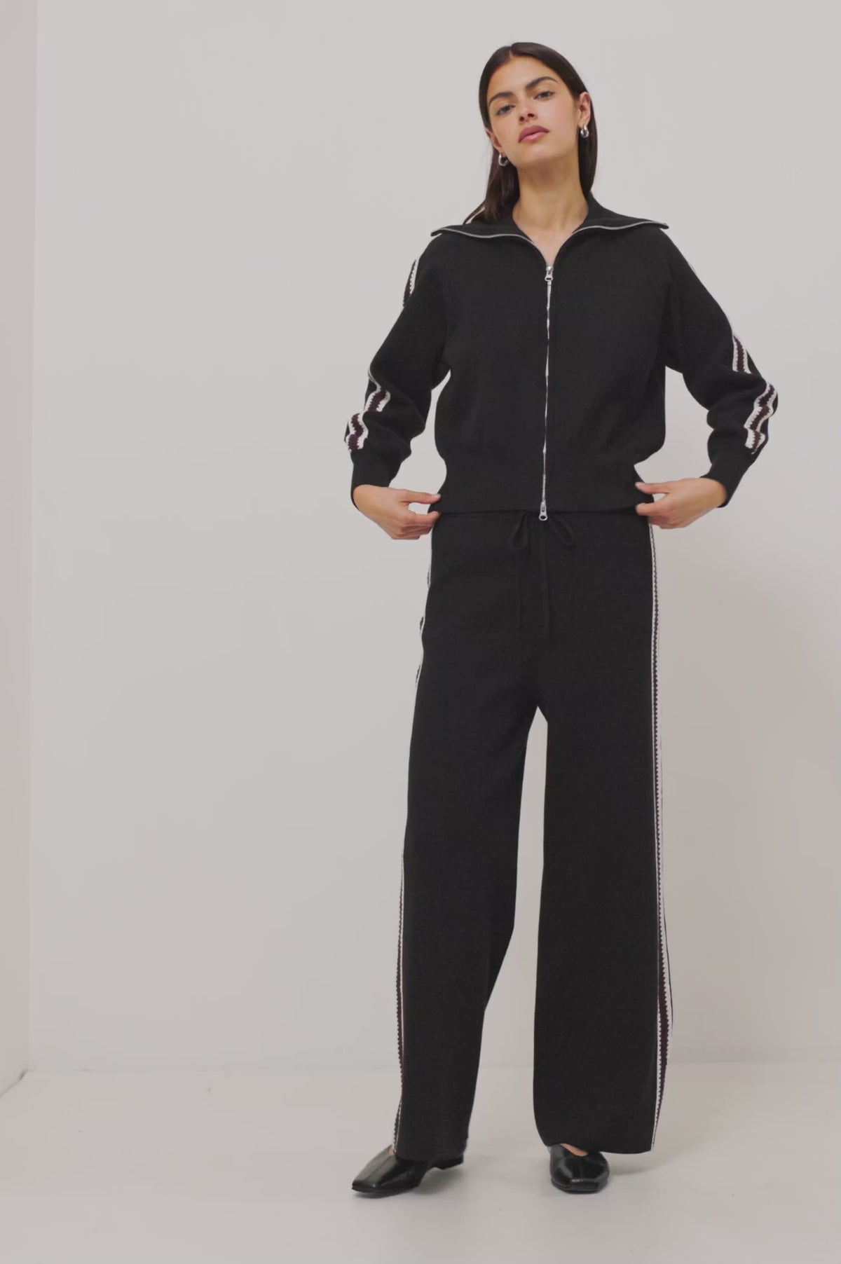 Tucker Pant in Soft Structured Knit With Wide Straight Legs, Drawstring Waist Ties, and Crochet Side Stripes in Black Merlot Stripe Colorway - Full Body View Featured on Model Moving (Video).