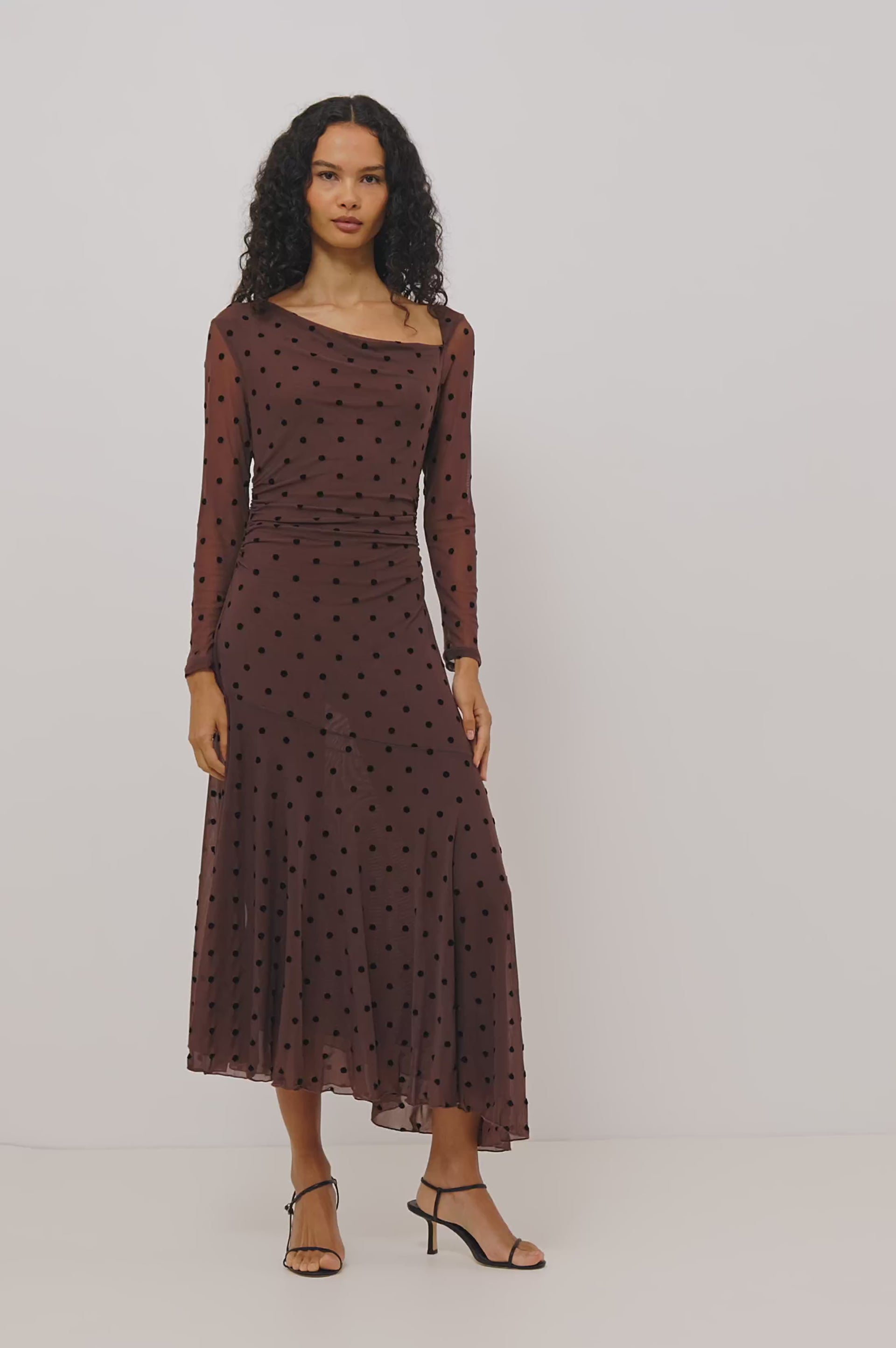 Cambria Midi Dress in Semi-Sheer Stretch Mesh With Velvet Polka Dots, Self-Lined Body, Asymmetric Cowl Neckline, Ruched Side Waist, and Softly Flared Skirt in Chocolate Polka Dot Colorway - Full Body Front View Featured on Model - Video