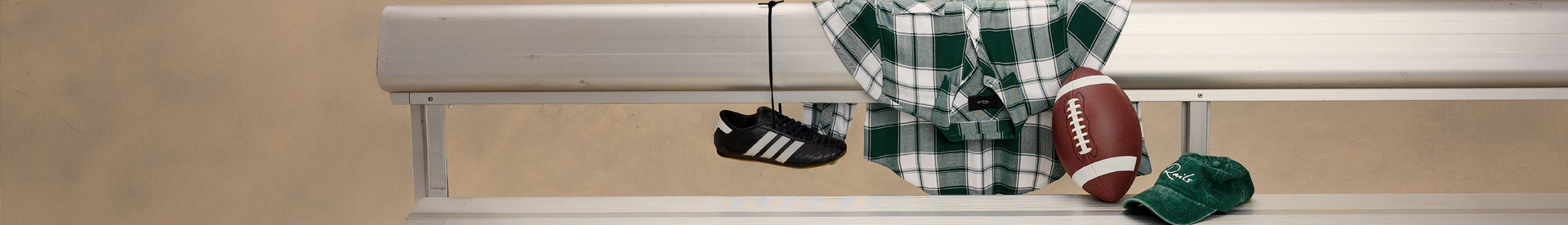 A horizontal banner-style graphic showing a beige wall and window trim with several sports items hanging from a hook: a black-and-white athletic shoe, a green-and-white plaid shirt, a brown football, and a green baseball hat.