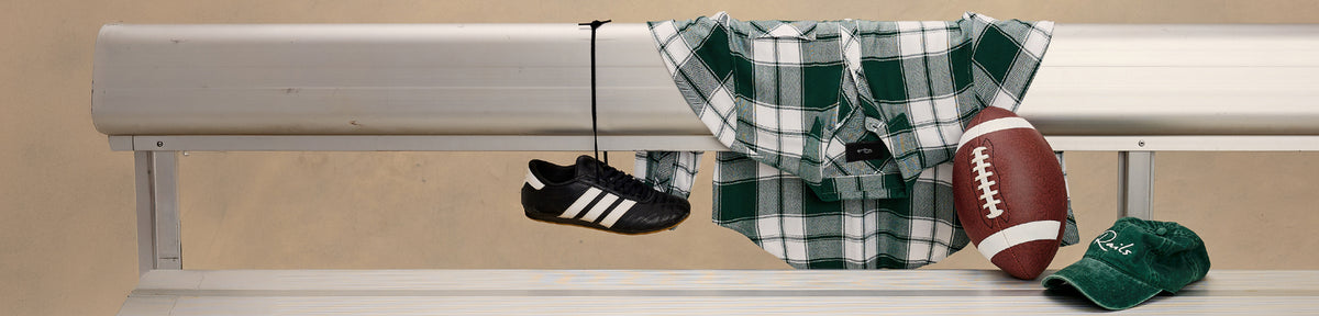 A horizontal banner-style graphic showing a beige wall and window trim with several sports items hanging from a hook: a black-and-white athletic shoe, a green-and-white plaid shirt, a brown football, and a green baseball hat.