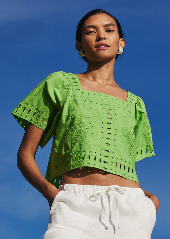 FRONT EDITORIAL IMAGE OF MODEL WITH HANDS IN THEIR POCKETS WEARING LAINE TOP IN ISLAND GREEN AND EMMIE PANTS IN WHITE