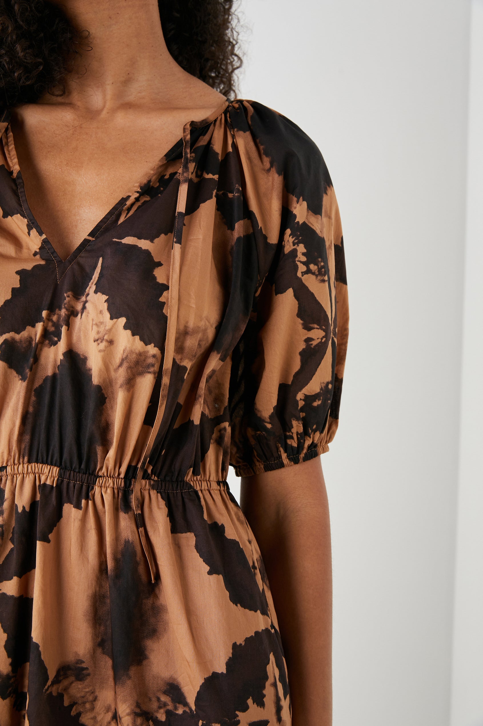 Amabella Short Sleeve Mini Dress with a V neck with Ties, Puff Sleeves, a Cinched Waist, and a Tiered Skirt in Tigers Eye Colorway, a Floral Pattern in Browns on Dark Brown - Front View Featured on Model  
