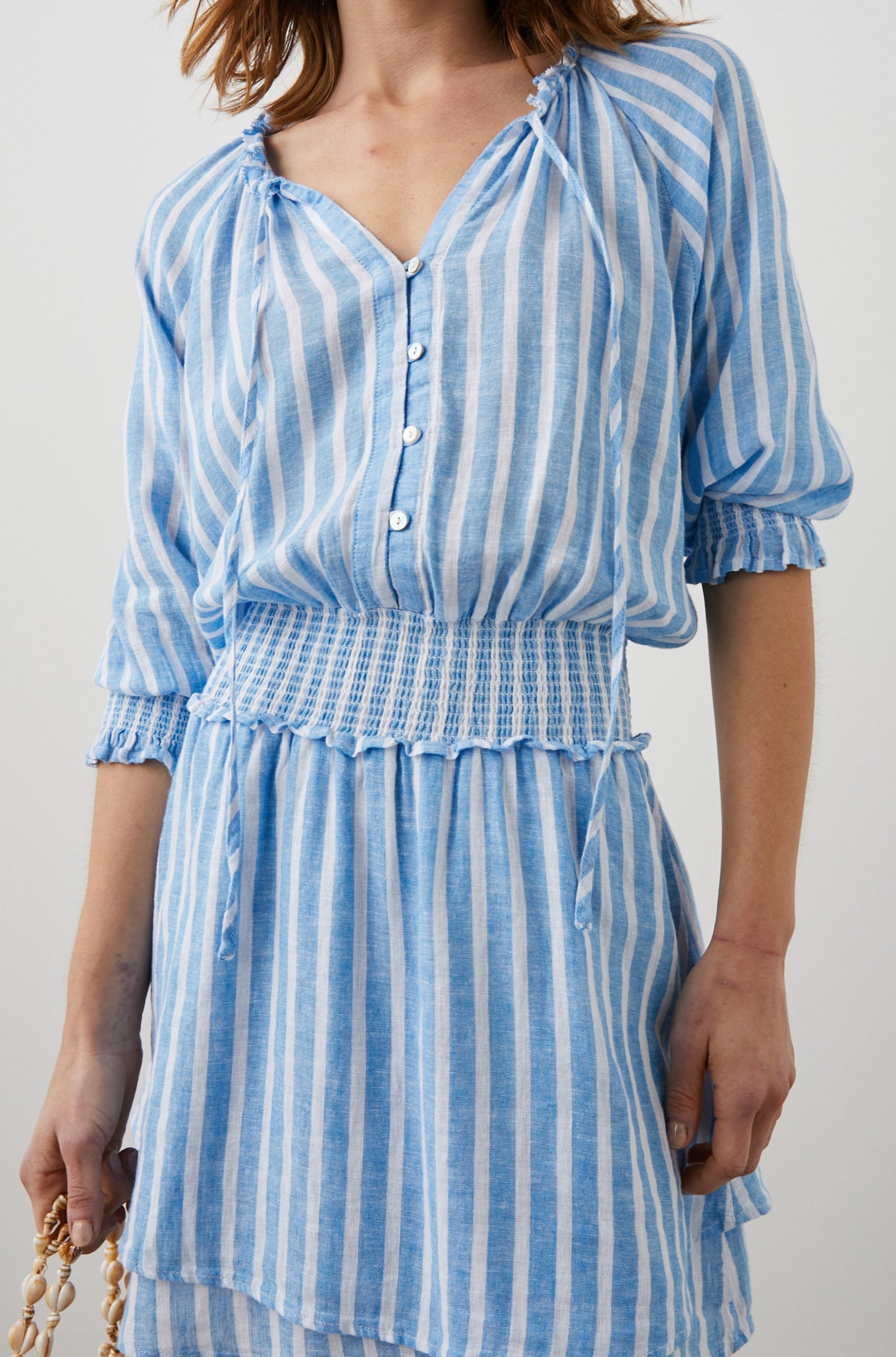 Crystal Mini Dress with Mid-Length Sleeves, Shirred Cuffs and Waist, a V Neck, Ties at the Collar, and Buttons down the Bodice in Lake Stripe Colorway, White and Blue Vertical Stripes - Front View Featured on Model 