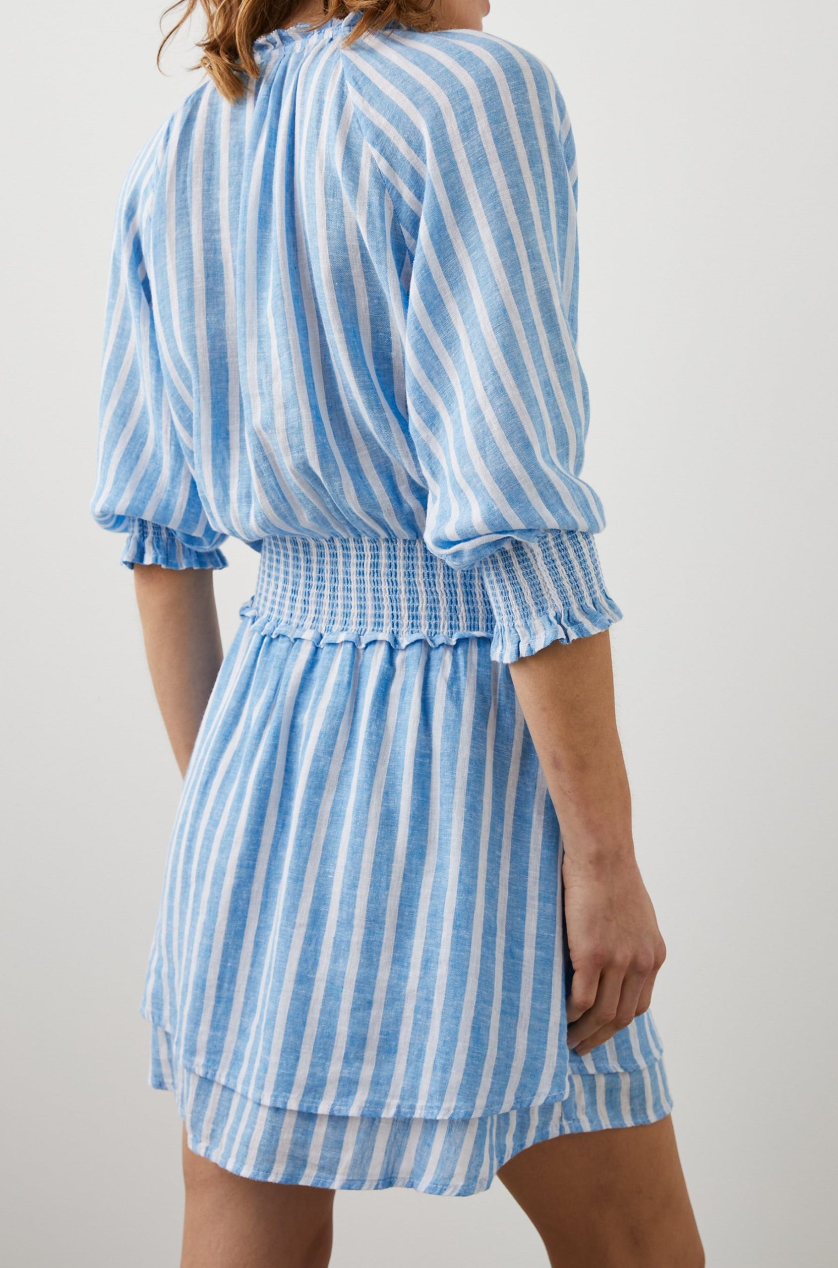 Crystal Mini Dress with Mid-Length Sleeves, Shirred Cuffs and Waist, a V Neck, Ties at the Collar, and Buttons down the Bodice in Lake Stripe Colorway, White and Blue Vertical Stripes - Back View Featured on Model 