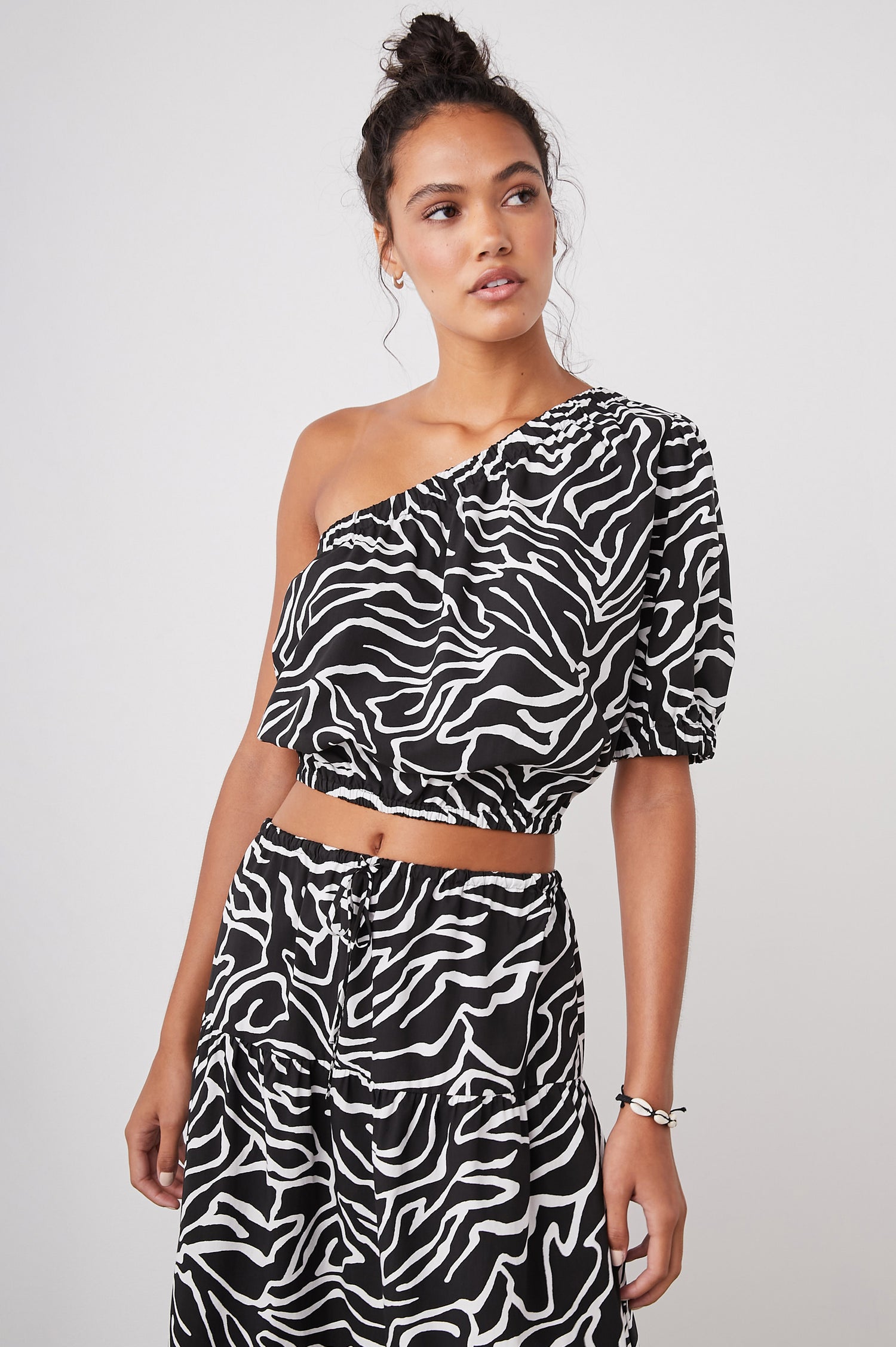 Evy Crop Top with an Asymmetrical Neckline, One Short Sleeve, and One Sleeveless, an Elasticized Hem and Cuff in Contour Lines Colorway, White Curves on Black - Front View Featured on Model 