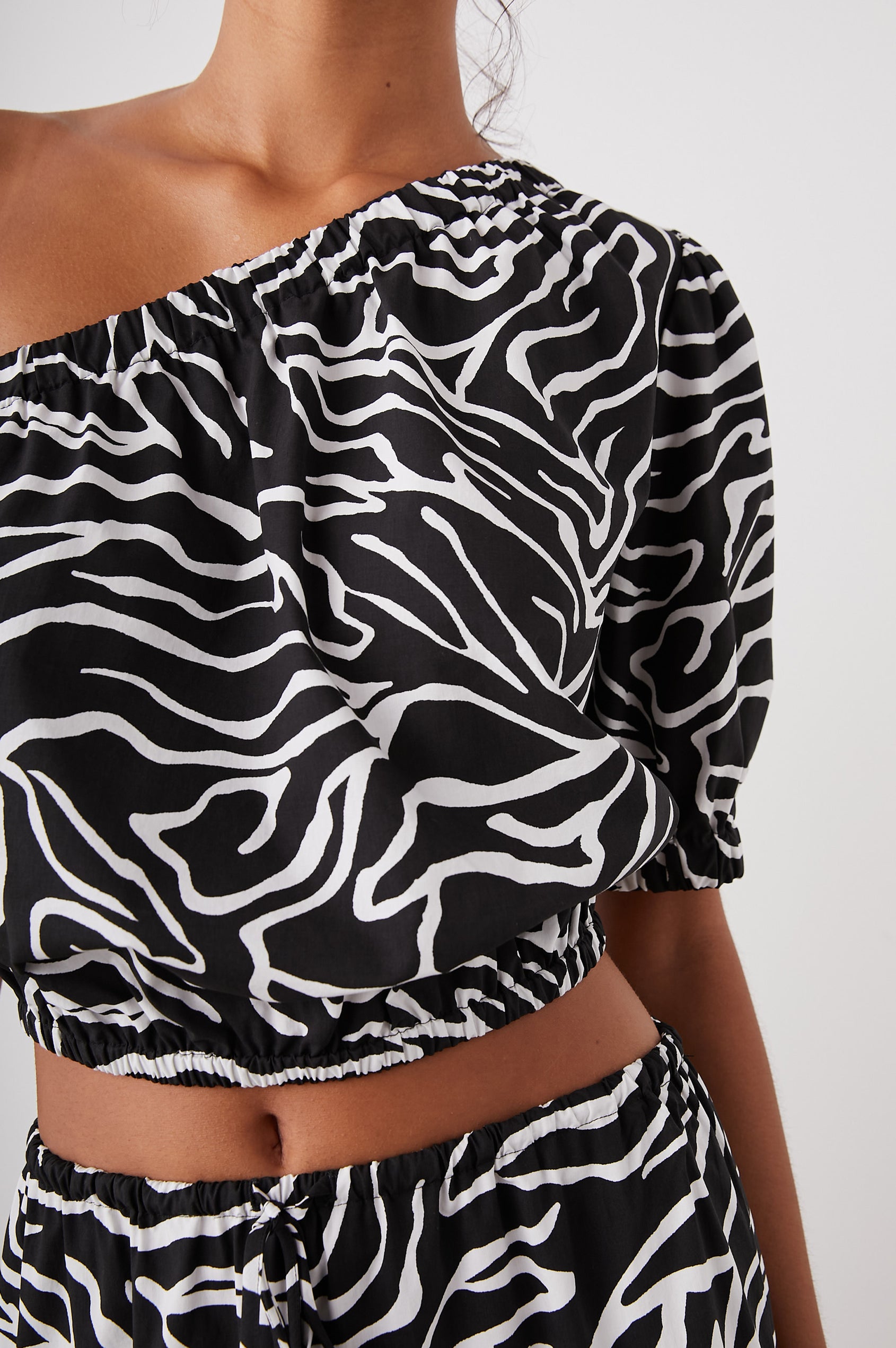 Evy Crop Top with an Asymmetrical Neckline, One Short Sleeve, and One Sleeveless, an Elasticized Hem and Cuff in Contour Lines Colorway, White Curves on Black - Front View Featured on Model 