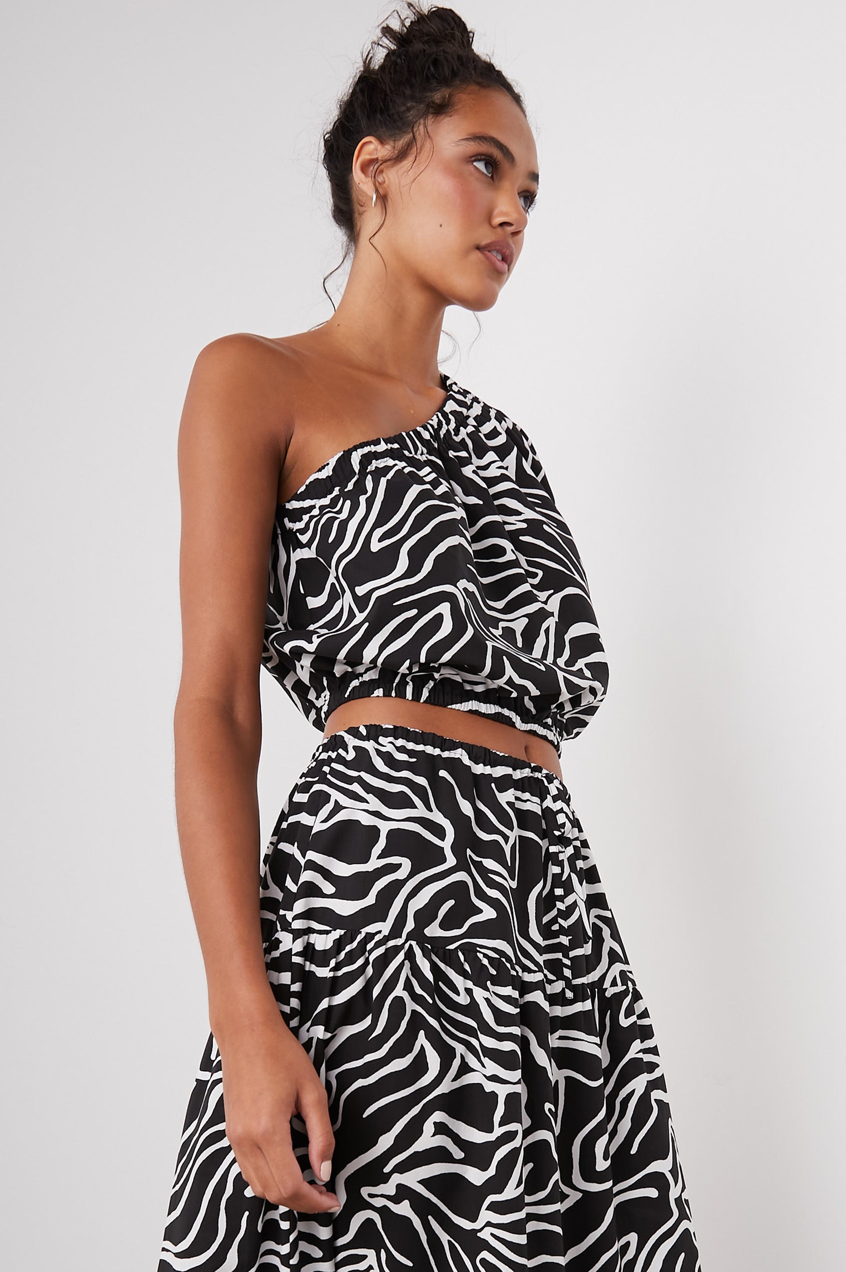 Evy Crop Top with an Asymmetrical Neckline, One Short Sleeve, and One Sleeveless, an Elasticized Hem and Cuff in Contour Lines Colorway, White Curves on Black - Side View Featured on Model 