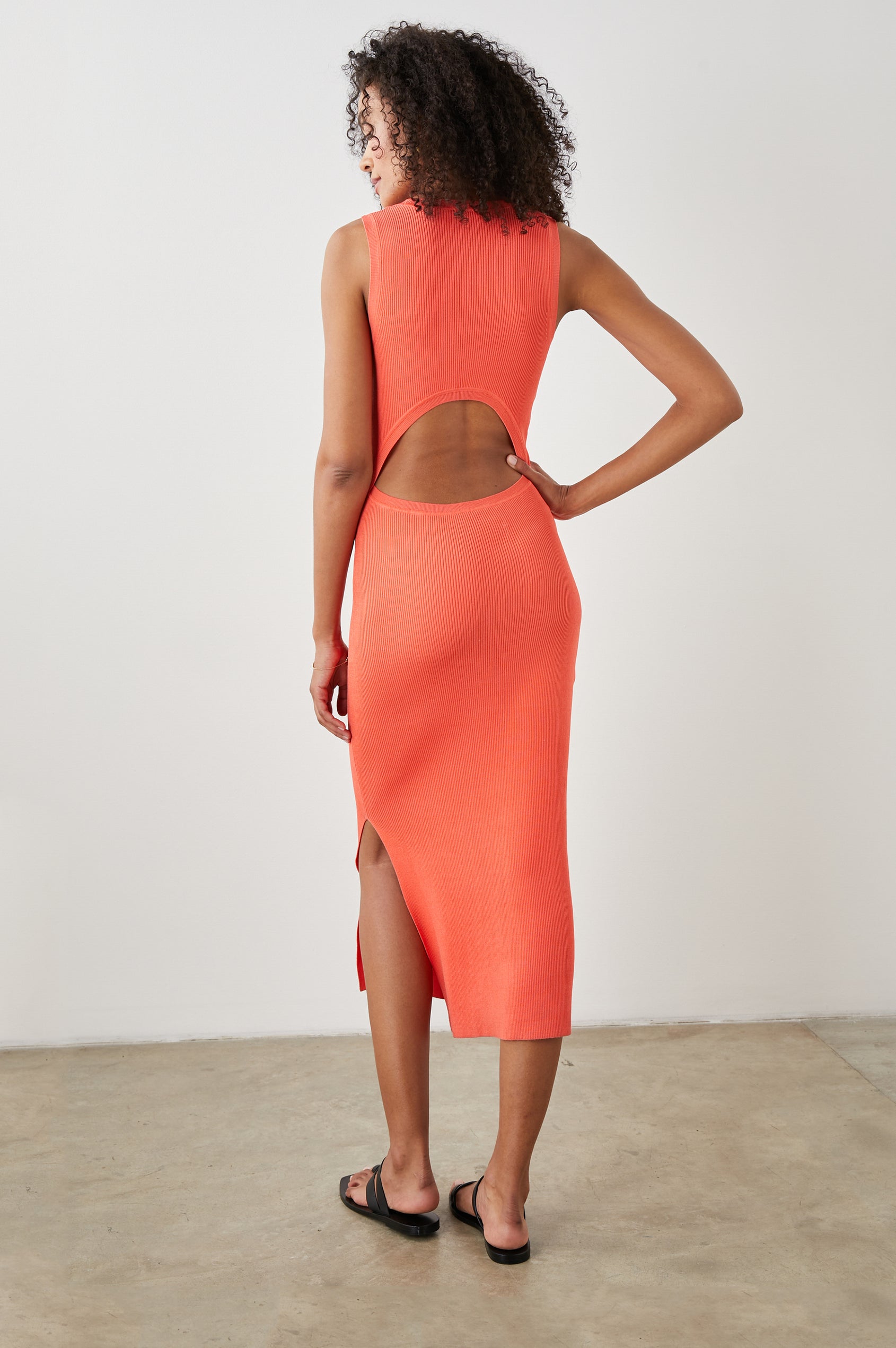Syd Ribbed, Sleeveless Midi Dress with Wide Shoulder Straps, a Side Slit, and a Cutout that Spans the Lower Back in Black Colorway - Back Full Body View Featured on Model  