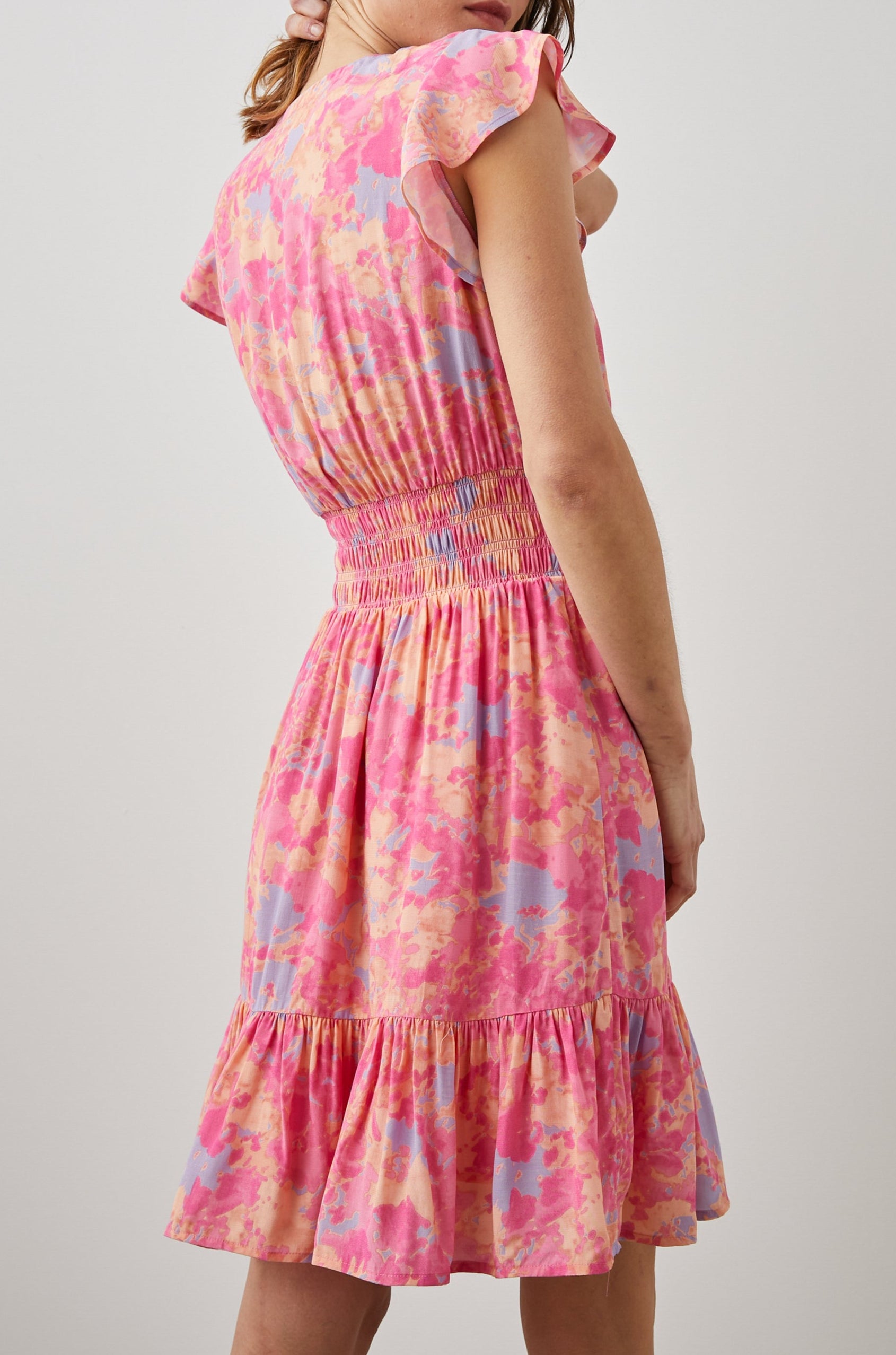 Tara Short Sleeve, Above the Knee Dress with a Smocked Waist, V Neck, Flutter Cap Sleeves, and Tiered Skirt with a Ruffled Hem in Passion Flower Colorway, in Pink, Yellow and Blue - Back View Featured on Model 